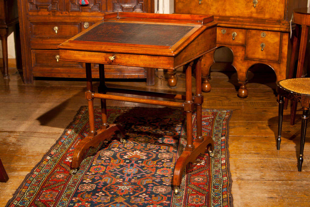 This desk features a gallery surround that walls off the ink and pen wells at the back area above the sloped and leathered writing surface.  Inside, two generously sized drawers offer additional storage for writing implements and erasers. The