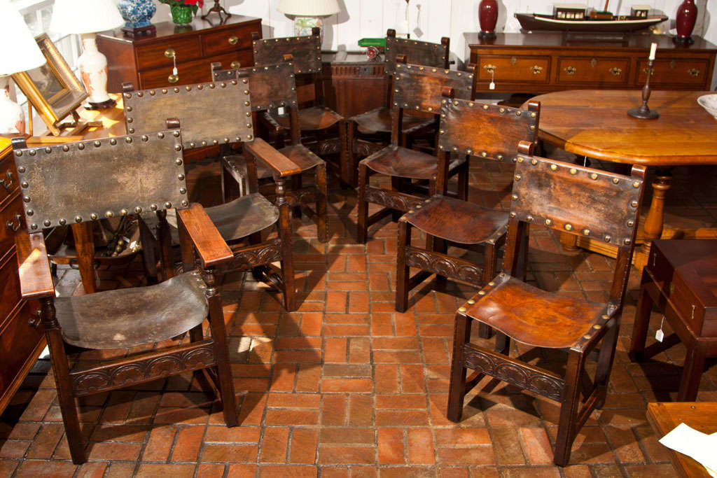 A set of 8 (2 arm chairs and 6 side chairs) English Jacobean Revival chairs with leather sling seats on oak and sycamore frames with hand carved decoration. These chairs are true to the Jacobean aesthetic and each features carvings that employ