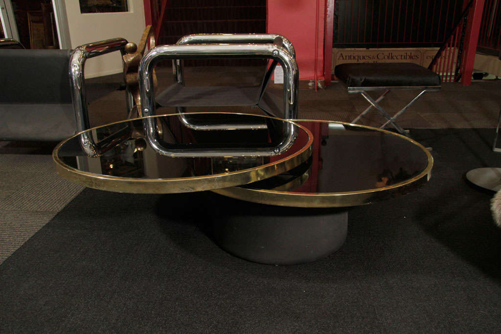 A mid century Italian glass top coffee table with brass accents and a metal base. The top round section is adjustable and can be aligned with the lower one for small spaces, or swiveled out for more surface area. Each circular surface is 36