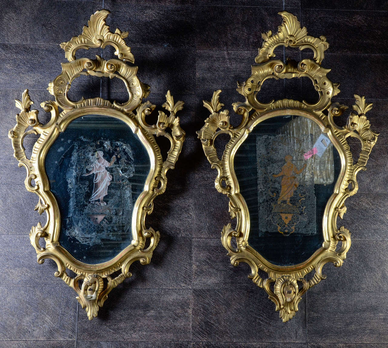 A rare pair of mid-18th century Venetian giltwood girandoles each surmounted by a stylized cresting supported by scrolls each in turn enriched with foliate carving. The mirror plates are original. The girandoles retain their original gilt tole