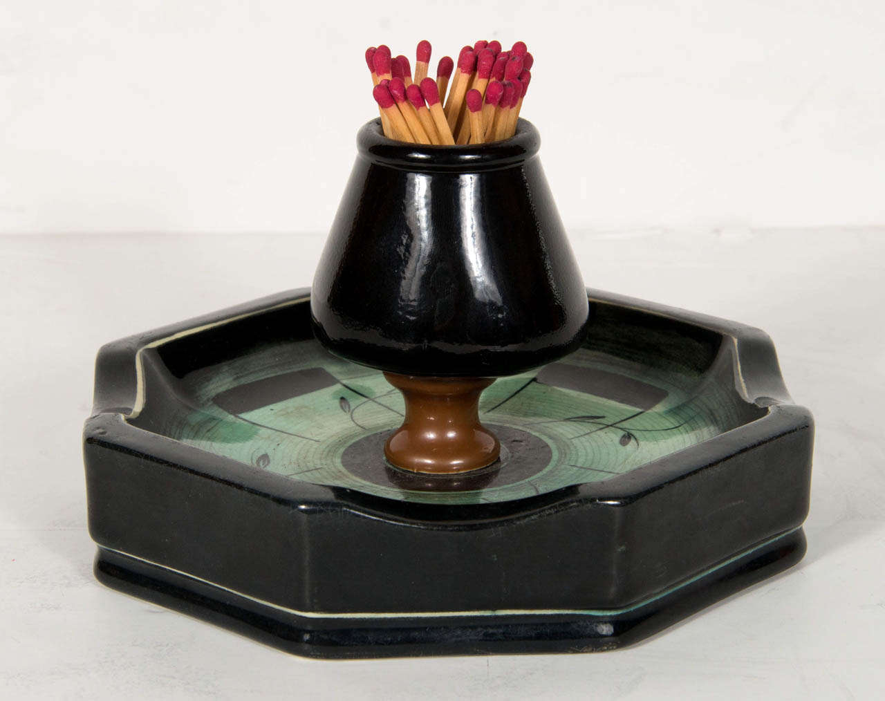 This unique match holder/ashtray by Ilse Claussen of Sweden in aqua blue green glaze has stylized hand painted Art Deco detailing. It has an octagonal shape with a central bowl in which matches are stored. It's signed on the bottom with Ilse