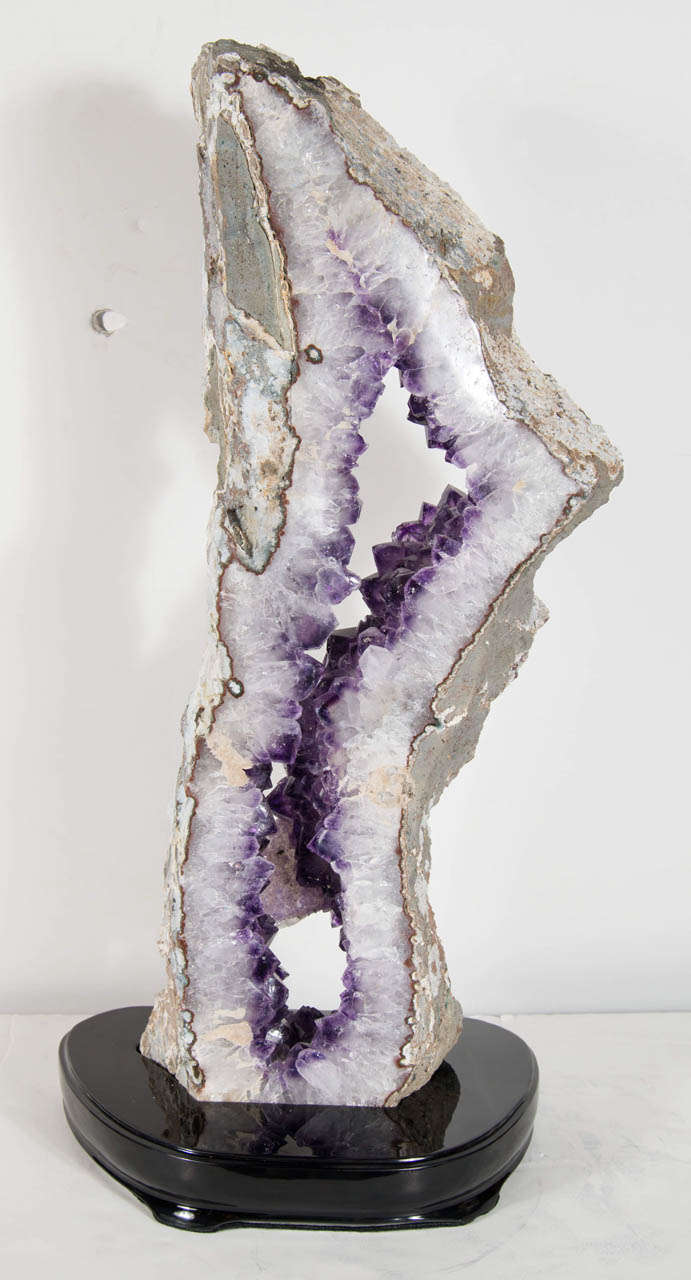 This monumental sliced geode mineral specimen of Quartz with an interior trim of brilliant colors has a beautiful elongated shape and features a core of dramatic Amethyst crystals that could set as a centerpiece in any design, it is also mounted on