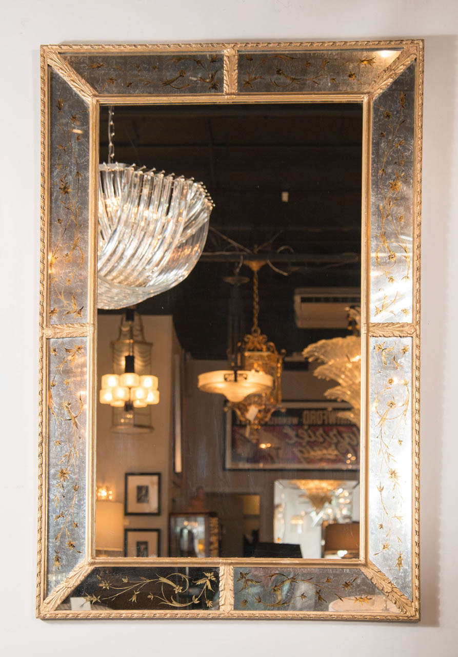 This exquisite Hollywood Regency Mirror features a rectangular shape with borders decorated with an eglomise guilded floral design on antiqued mirror and  stylized gilt laurel and ribbon details.can be hung vertically or horizontally.
