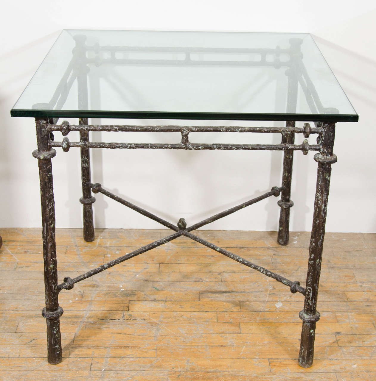 A vintage Diego Giacometti style cast iron X-base table with a decorative bird sitting on the cross bar stretchers and glass top. Good vintage condition with age appropriate patina.