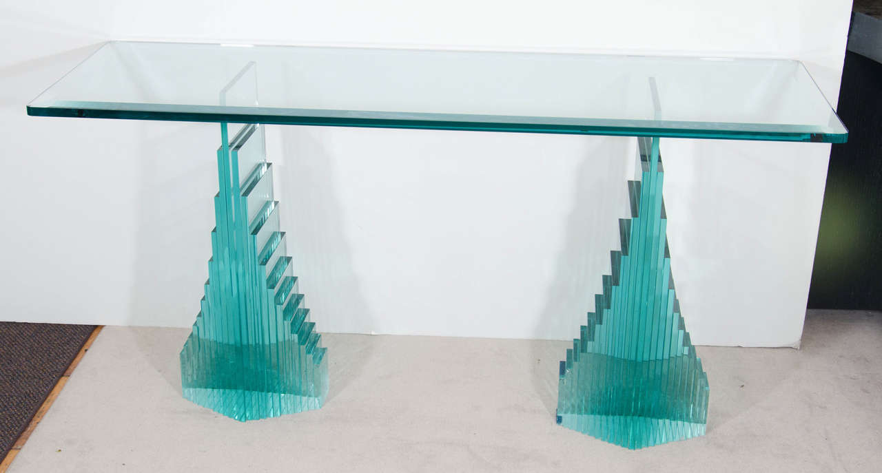 A vintage console table with a unique and heavy base made of stacked and stepped rectangular glass. The table has a 3/4