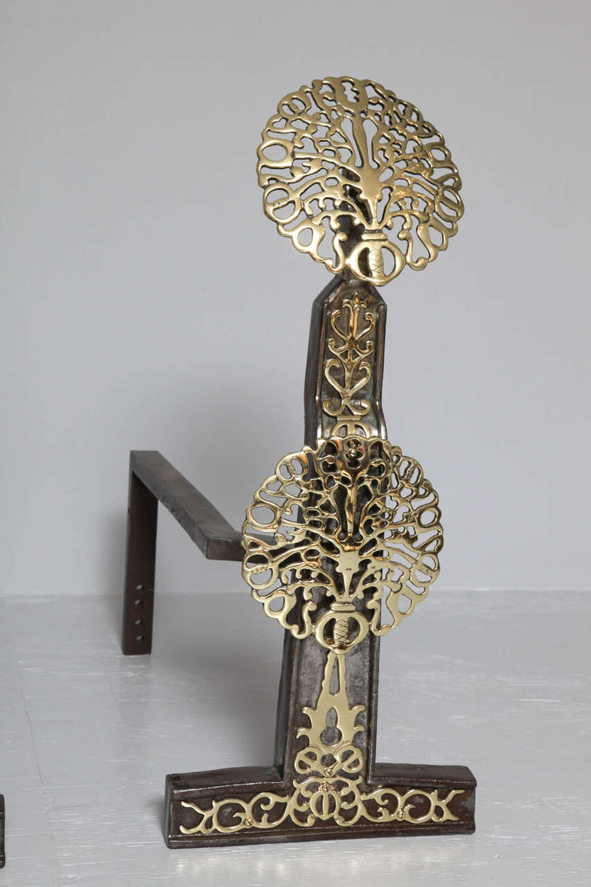 An exceptional pair of English andirons, possibly by Ernest Gimson having double blossom brass bosses applied to and iron backing, the shaft having similar applied pierced decoration, all of very fine quality. See the Cheltenham Museum collection of