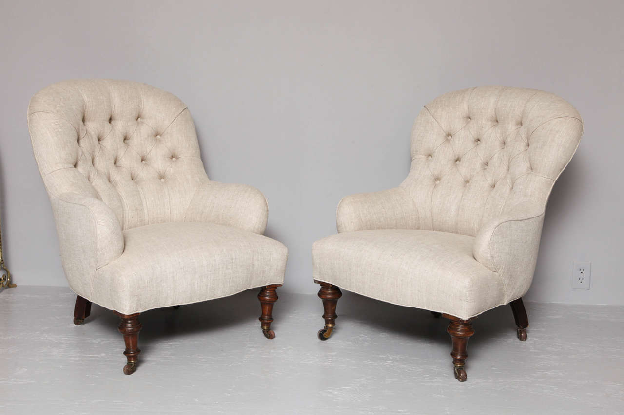 Fine matched pair of 19th century English club chairs having rounded tufted backs, scrolled arms and shaped seats, newly upholstered in buttoned linen, standing on turned walnut legs with original brass and ceramic castors.
Note: slight variation