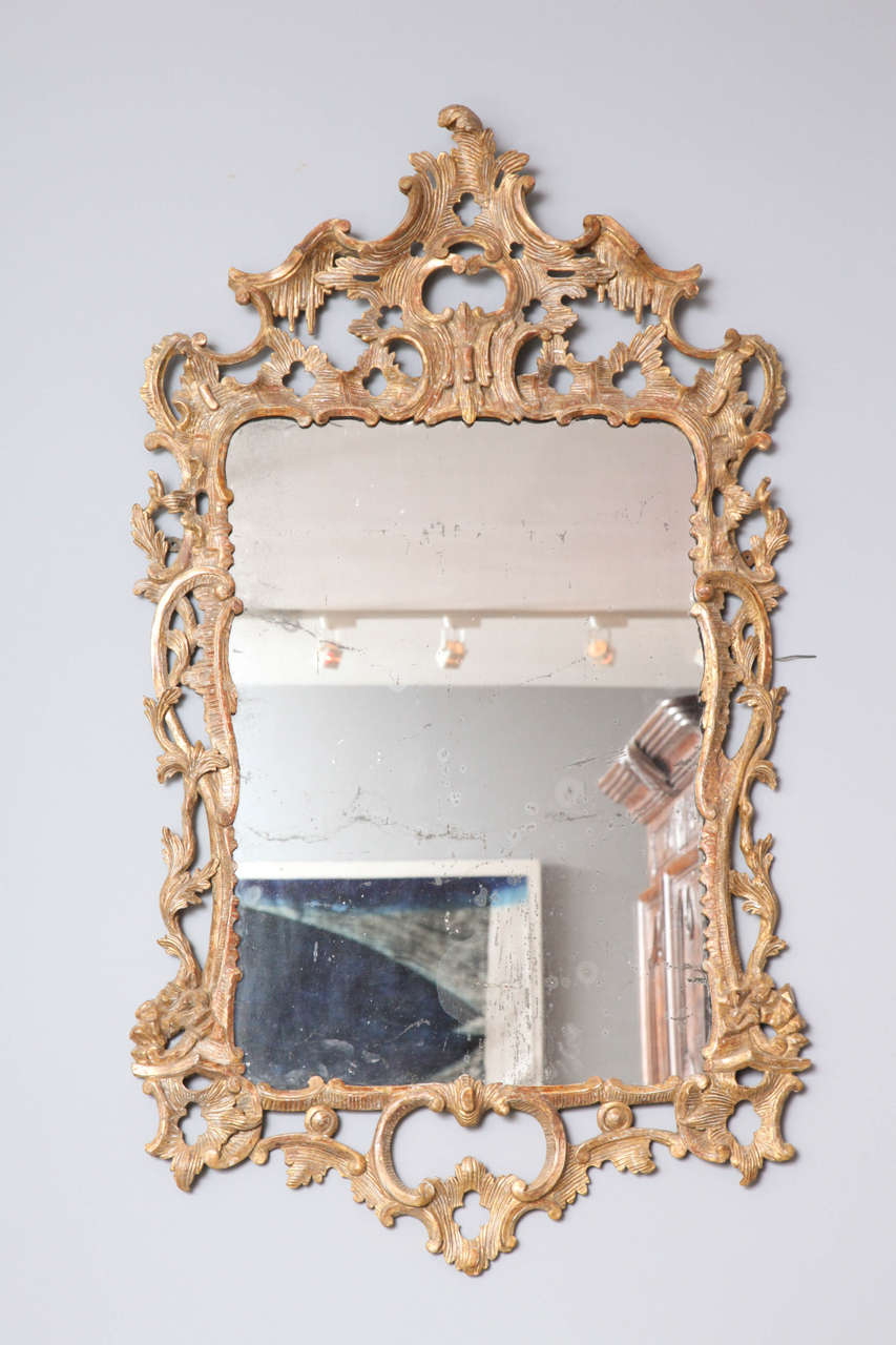 Specchio rococò in legno dorato intagliato di eccellenti proporzioni, con la cresta di un acanto stilizzato intagliato a Rocaille con volute a C e a S che decorano i lati e il fondo, il tutto con una bella superficie sfregata e brunita e che