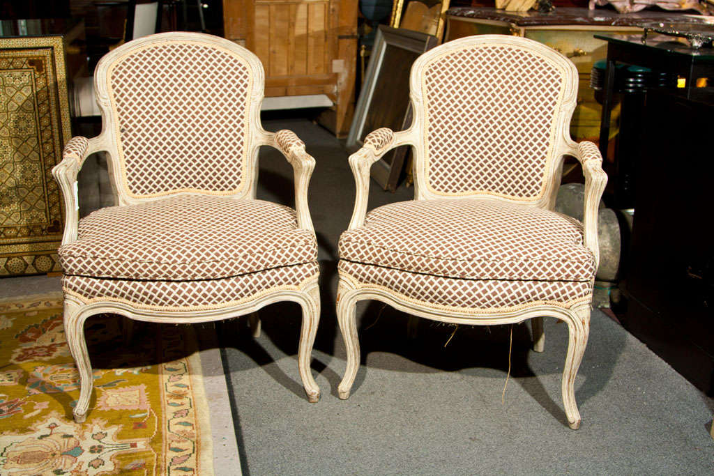 Pair of French Louis XVI style crème peinte fauteuils, circa 1920s, upholstered in back, arm rests, and cushioned seat, raised on cabriole legs.
