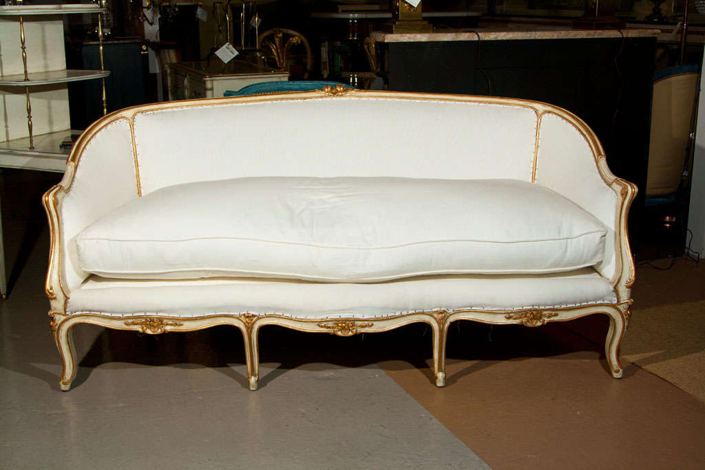 Elegant French Louis XV style sofa, circa 1940s, the creme peinte frame with parcel-gilding, upholstered in linen, padded back and cushioned seat, raised on cabriole legs. By Maison Jansen.