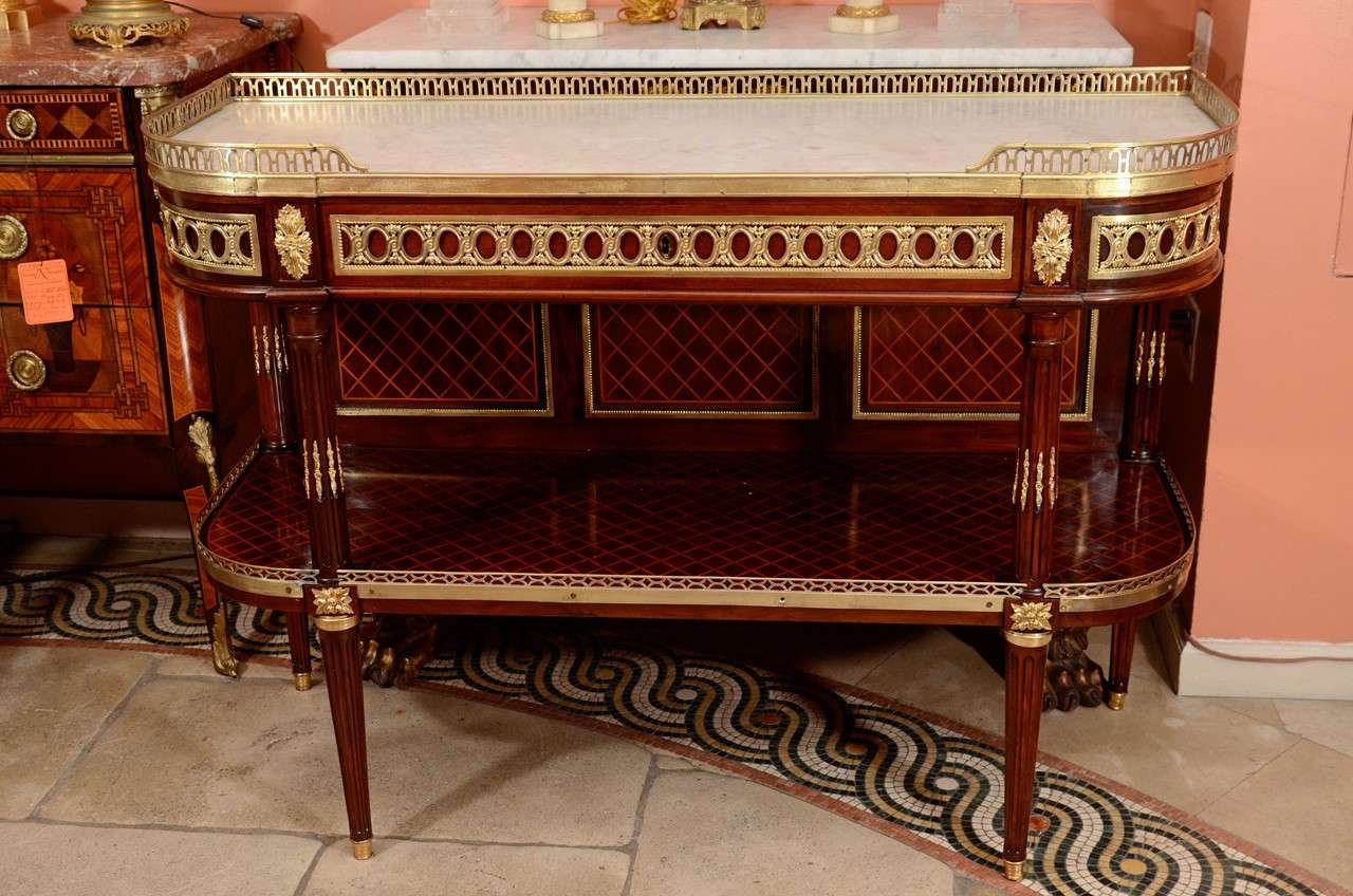 A fine Louis XVI marble-top mahogany console desserte. With a pierced bronze gallery, bronze mounts, lattice inlays and stop fluted supports.