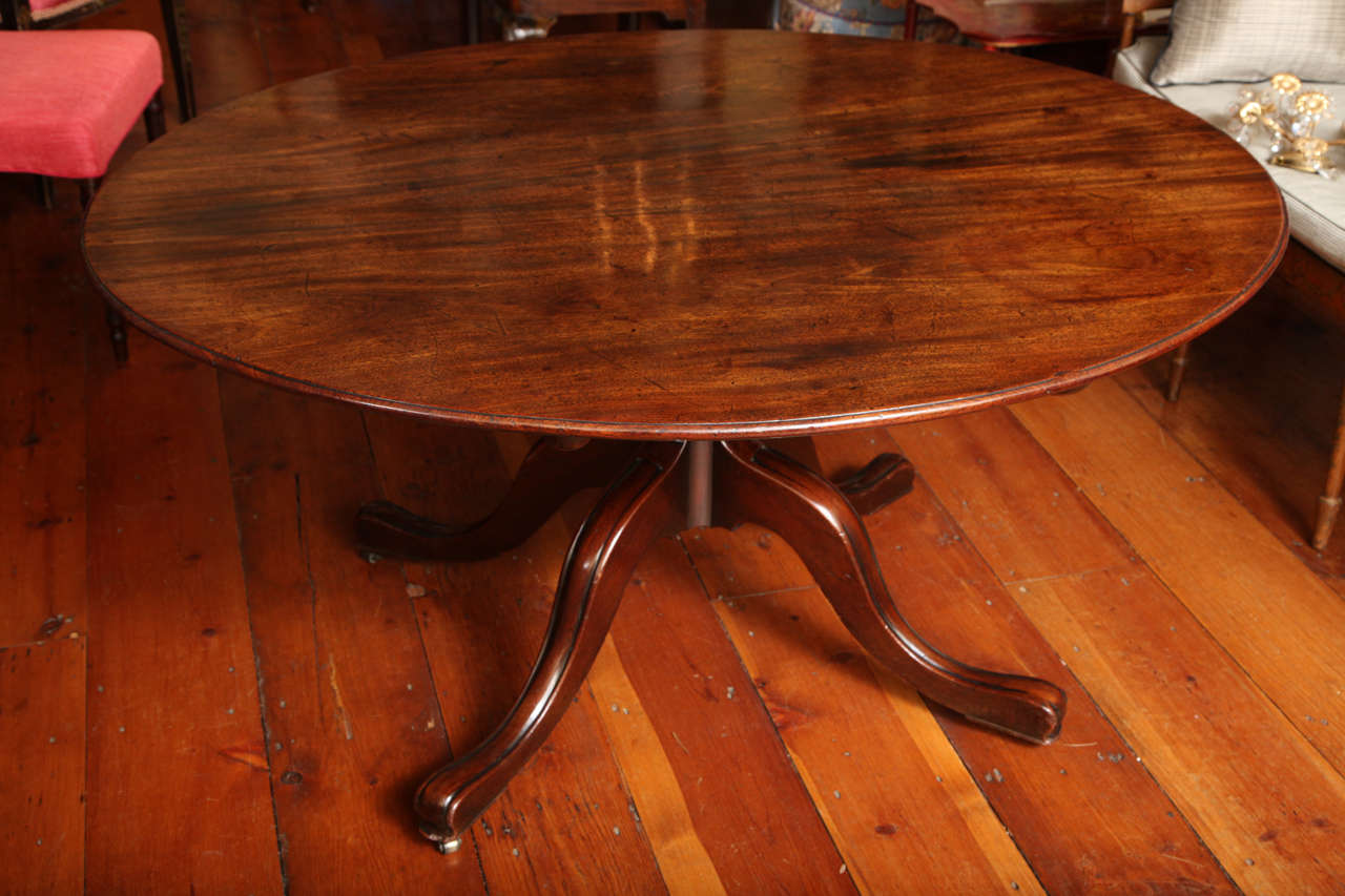 A beautifully drawn George III oval mahogany tilt-top breakfast table of the finest color and patination, having a thumb moulded top above a gun barrel stem and quadruped base with moulded cabriole legs ending in rounded pad feet with brass castors.