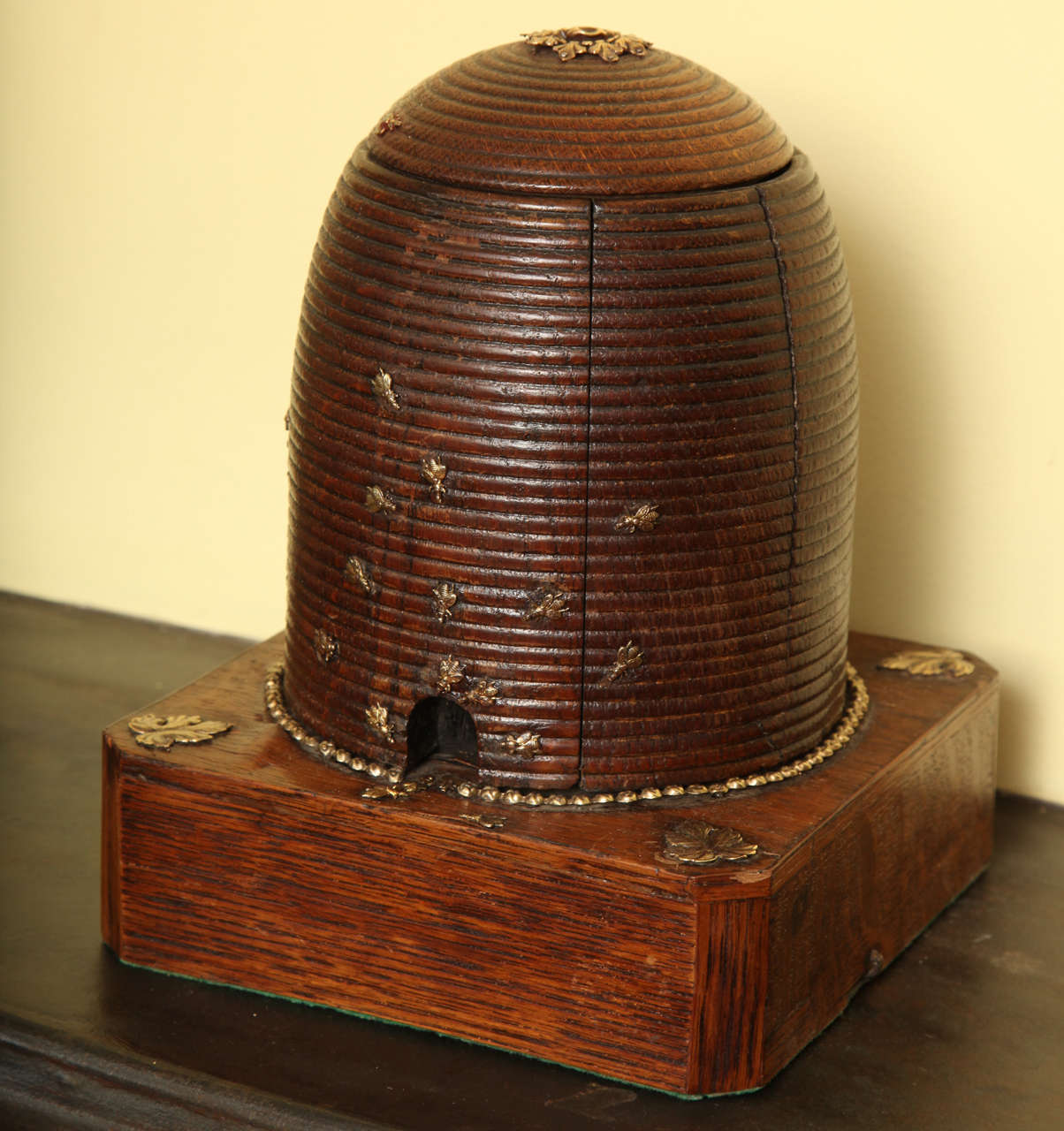 Victorian Carved Oak Beehive Form Cigar Holder,the square plinth base with canted corners and foliate appliques to the corners and top of the hive, having a solid ring ofbrass beading around the base of the hive and an assortment of stamped brass
