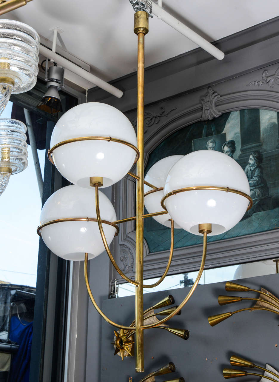 Nice chandelier made of a brass structure supporting four white glass globes that diffuse the light. In the style of the Lydon chandelier designed by Vico Magistretti in the 1970s for O'luce.

Perfect condition, new electrification.