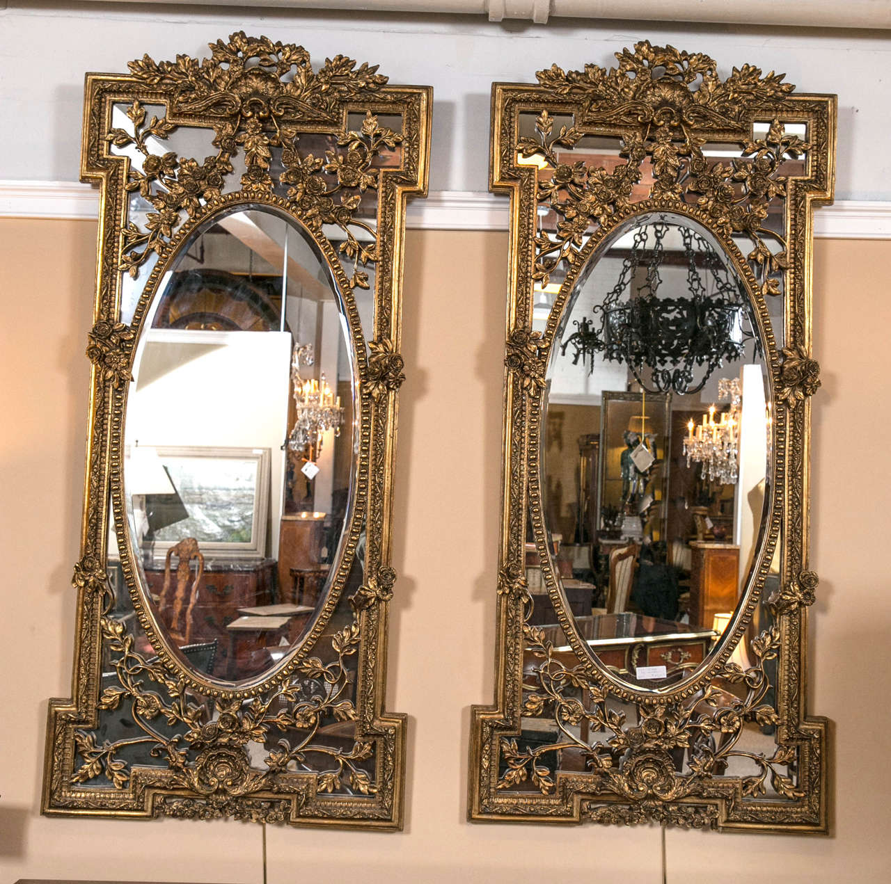 Pair of lovely giltwood and gesso beveled wall console mirrors in the Belle Époque style, second quarter of 20th century, the oval center beveled panel with annulated molding surmounted by elaborately carved rectangular reeded frame, decorated with