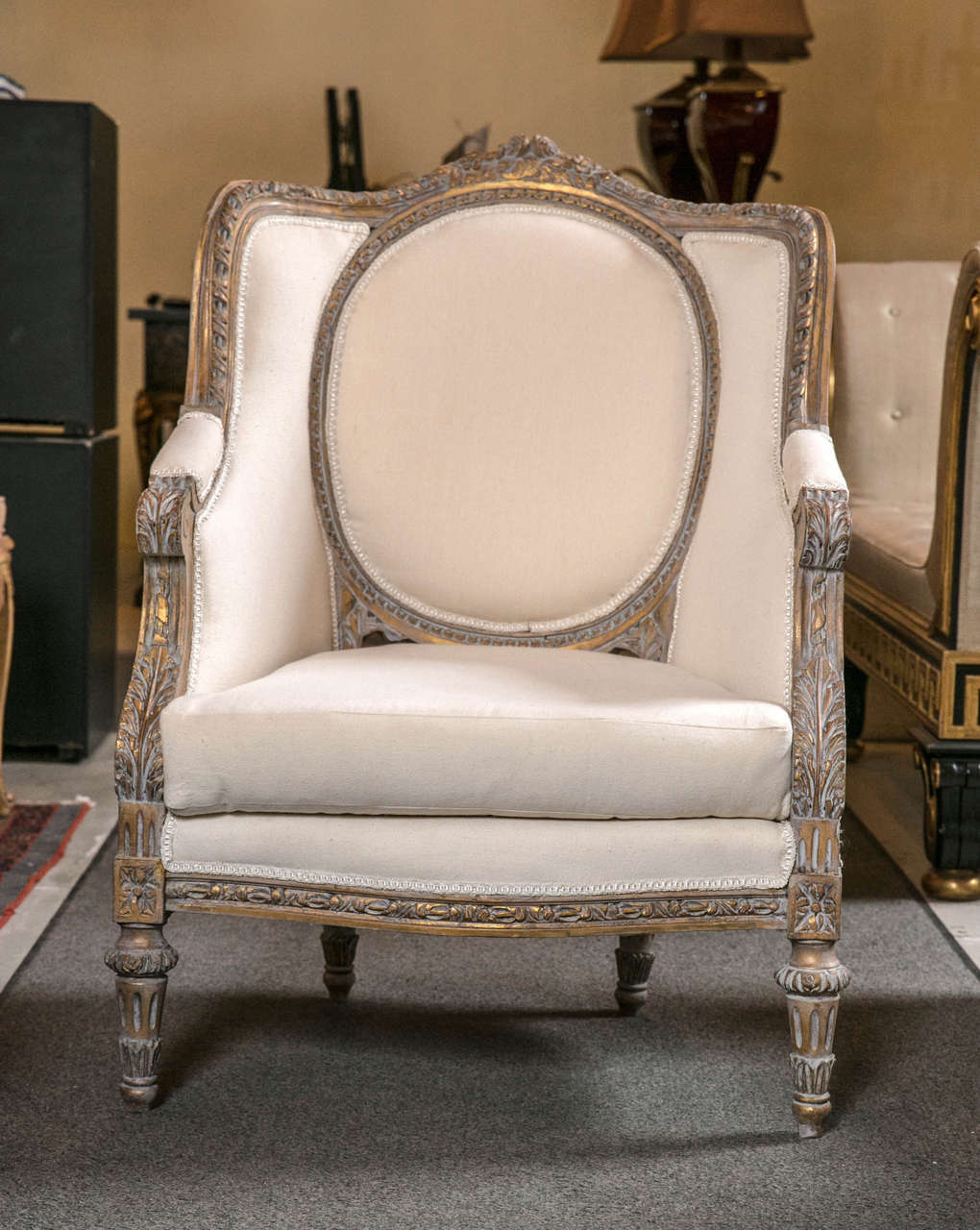 A beautiful pair of vintage French Louis XVI style bergere chairs, decorated in this gorgeous distressed gilt frame with a touch of grey, medallion back and downswept arms, joint by cushioned seat, raised on fluted tapering legs.