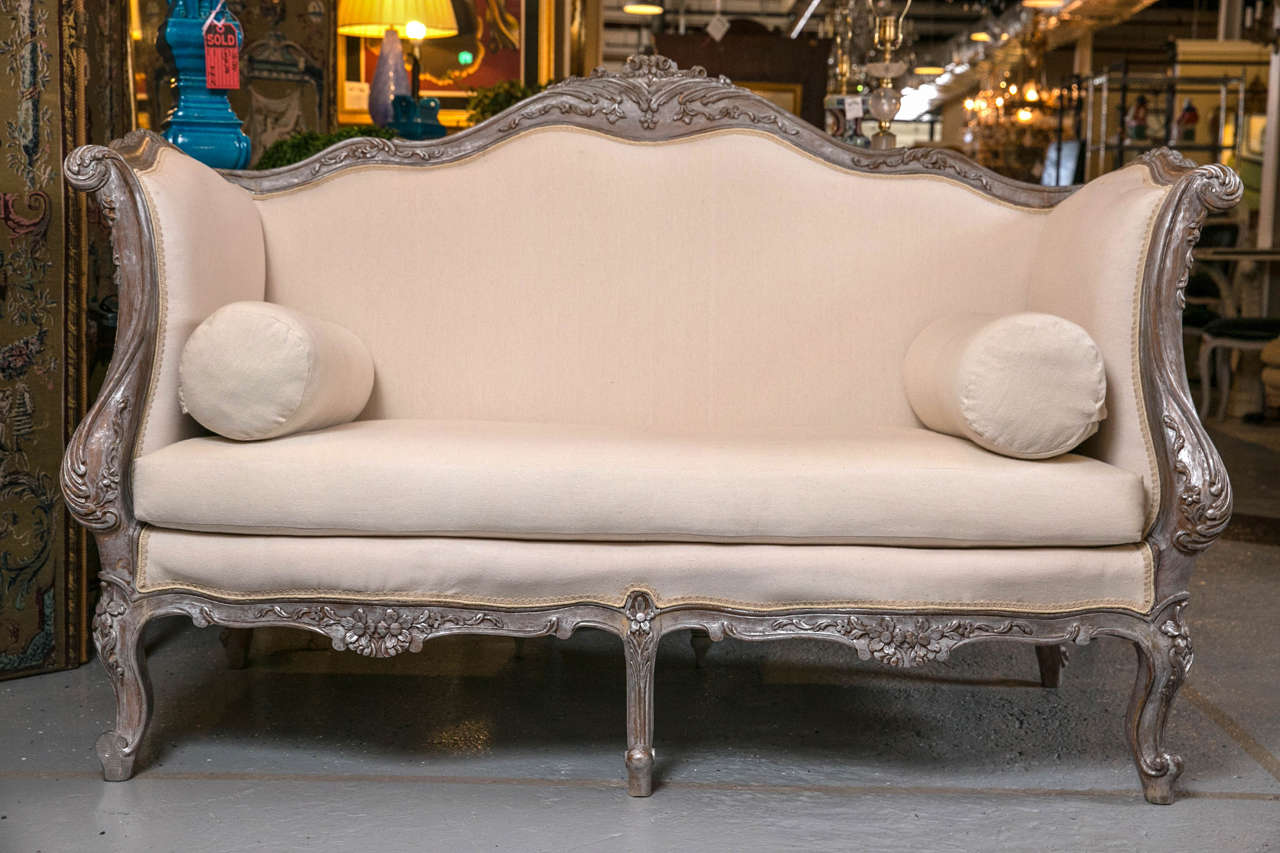 An alluring vintage French settee in the Rococo taste, second quarter of 20th century, the original intricate acanthine carving decorated with distressed silver gilding, the domed back-frame extending to scrolled arms, joint by a serpentine-shape