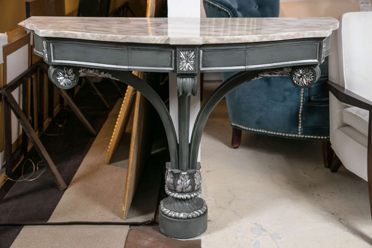 A Hollywood Regency demilune marble-top console table. This finely constructed console table, having a demilune shape with a shaped white marble atop a dark grey painted and silver-gilt plume-form base, the frieze fitted with a single drawer,