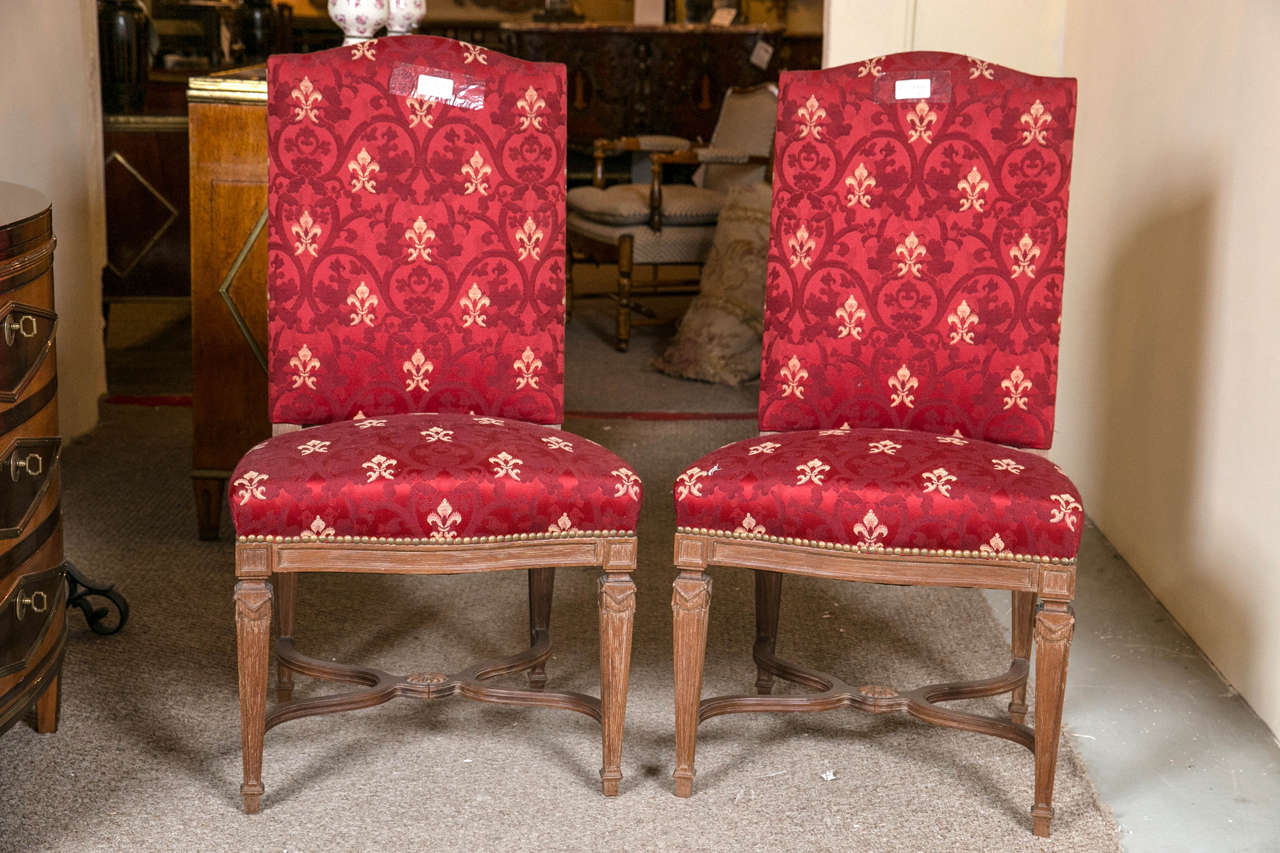 Pair of French Louis XVI style side chairs by Maison Jansen. The fine 20th century, distressed walnut frame, upholstered back and seat in red satin with fleur-de-lis embroidery, raised on fluted legs joint by an X-stretcher. The legs tapering and