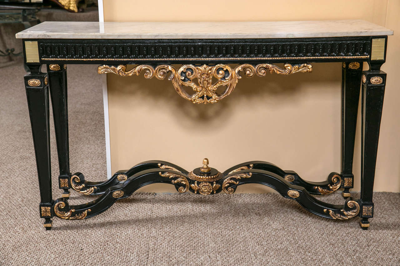 A charming French console table in the Rococo style, circa 1940s, overall ebonized and parcel-gilt, a shaped white marble atop a reeded frieze above an pierced scrolling crest, supported on four squared tapering legs joint by an ornate X stretcher