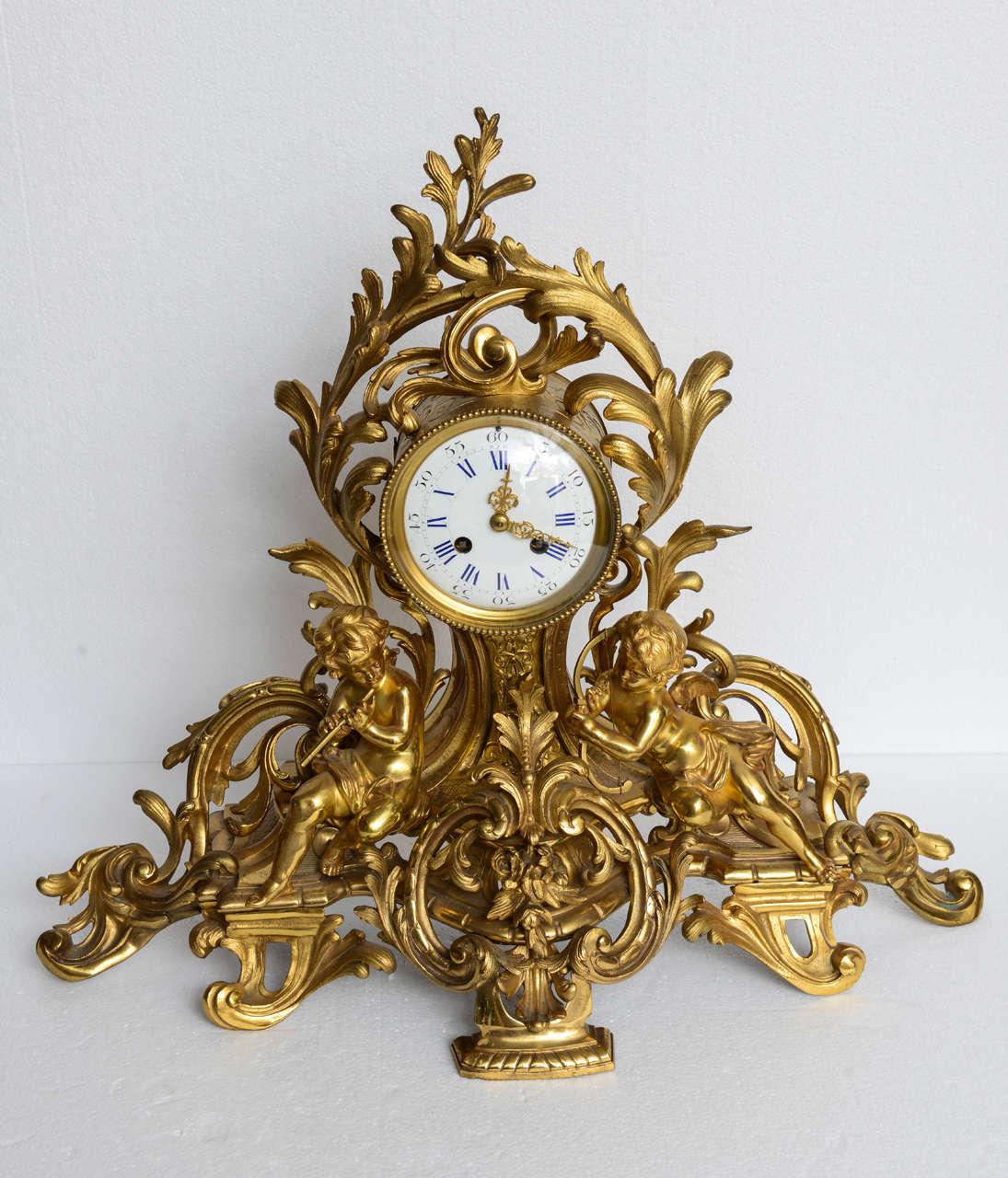 A near PAIR of French Louis XV mantel clocks with putti; finely cast with musical putti sitting on a rocaille form base, original restored finish, clock is working and keeps good time. They are identical with exception of the bezel which are very