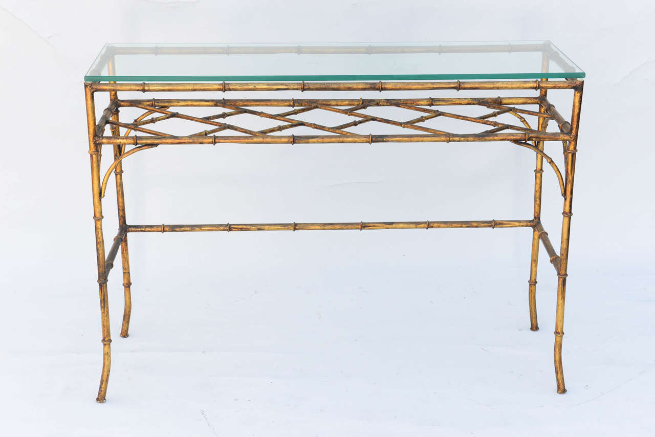 Console table having a rectangular glass top, on faux bamboo table, of gilded iron legs and fretwork shelf.