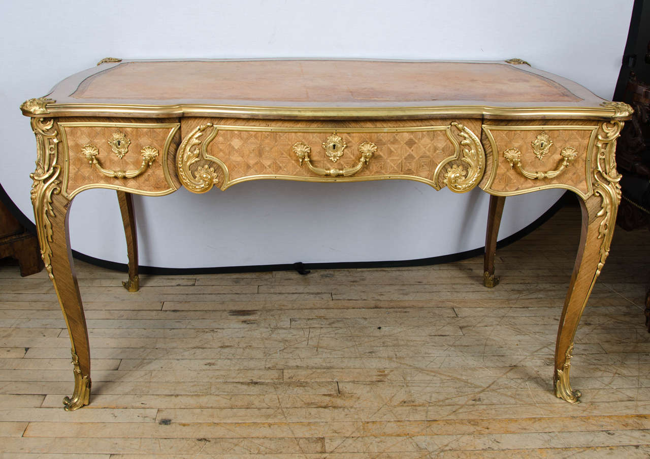 An outstanding quality French Louis XV style Kingwood Bureau Plat with an inset leather top with elaborate and detailed bright ormolu mounts that surround the table. There are three frieze drawers each with Parquetry inlay on one side and 3 false