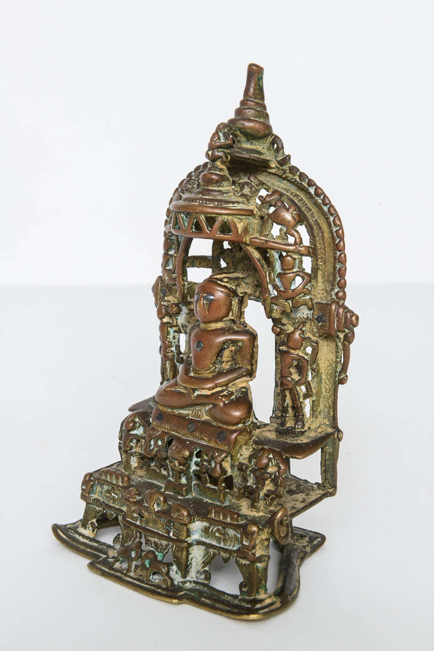 This serene Jain altarpiece of the enthroned and unclothed Buddha with numerous attendant figures including elephants is characteristic of Jain bronzes from the 15th century. The extensive inscription of the reverse is in Devanagari script with a