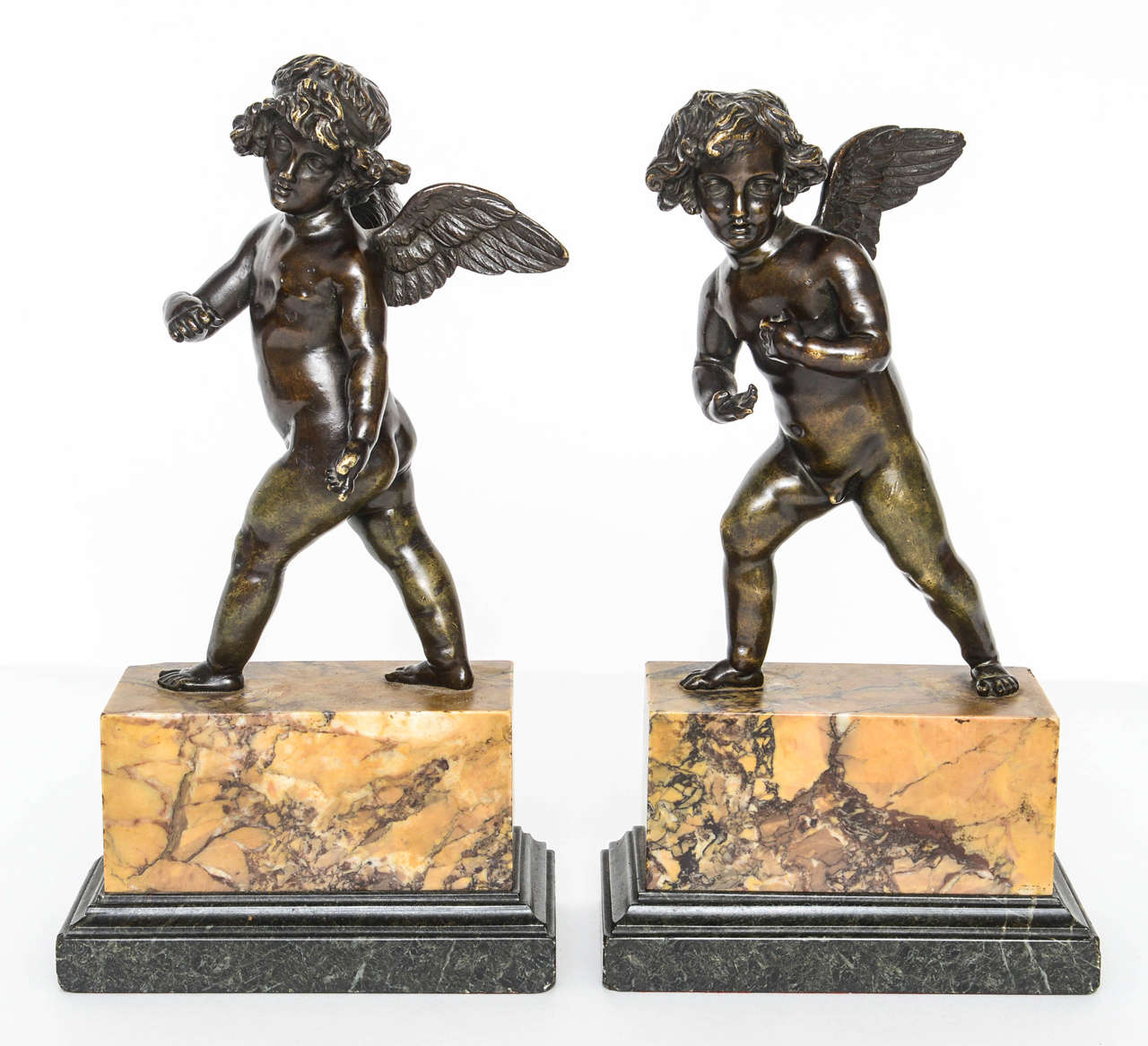 This handsome pair of bronze striding cupids are mounted on siena and green serpentine marble bases.  Each cupid is unique.

They are in the style of the French neoclassical sculptor Pierre Philippe Thomire  (1751-1843)