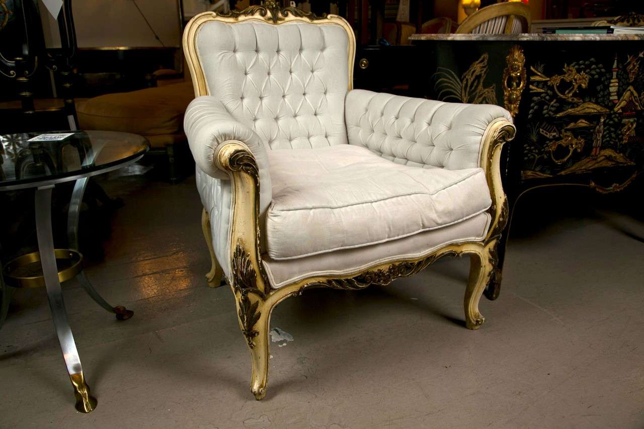 Pair of French Rococo style bergere chairs, circa 1940s, distress-painted and parcel-gilt frame, upholstered in white linen, tufted back and arm rests, cushioned seat, raised on cabriole legs.