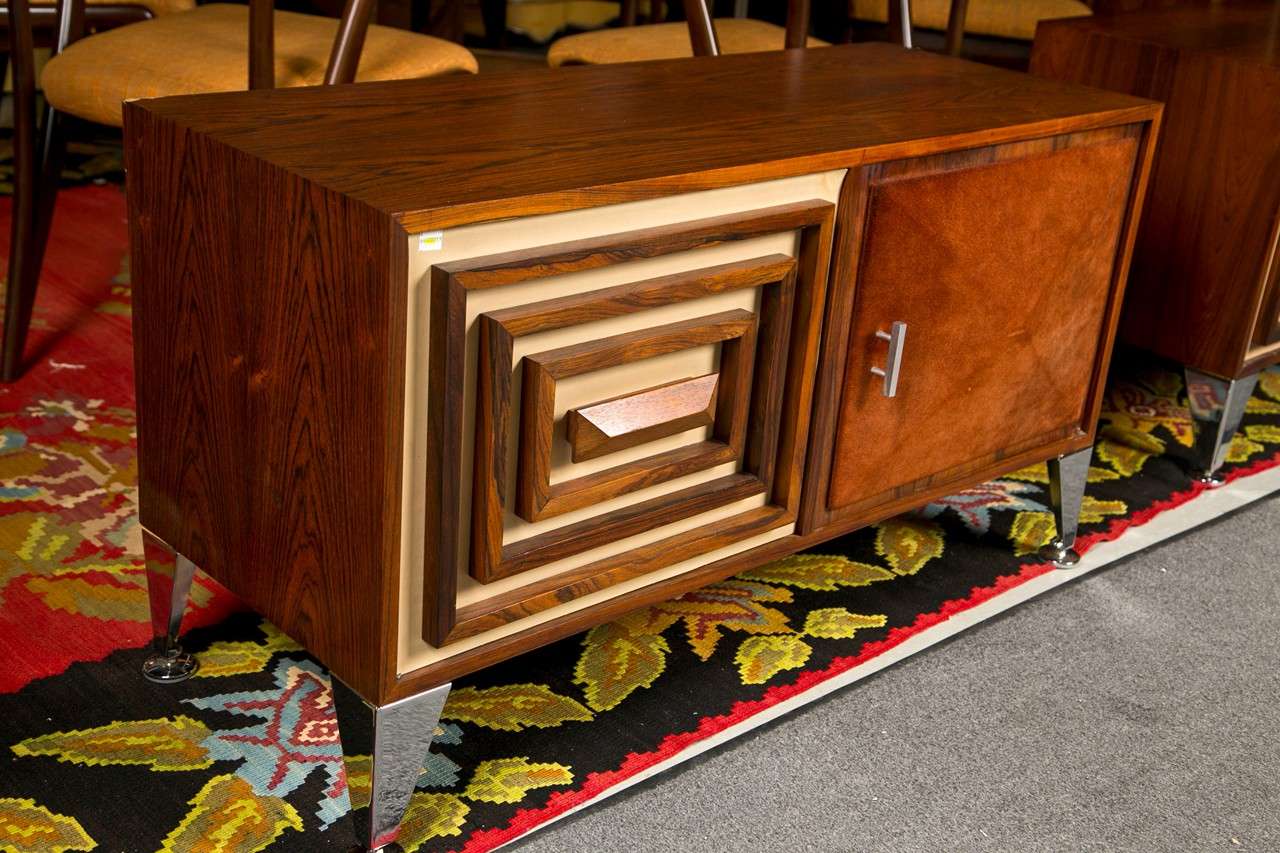 Pair of Mid-Century Modern credenzas:
Mahogany credenza commode, each with two cabinet doors, one with a suede covered convex diamond panel, the other with graduating wood frames surrounding the central door handle. Raised on tapering chrome bracket