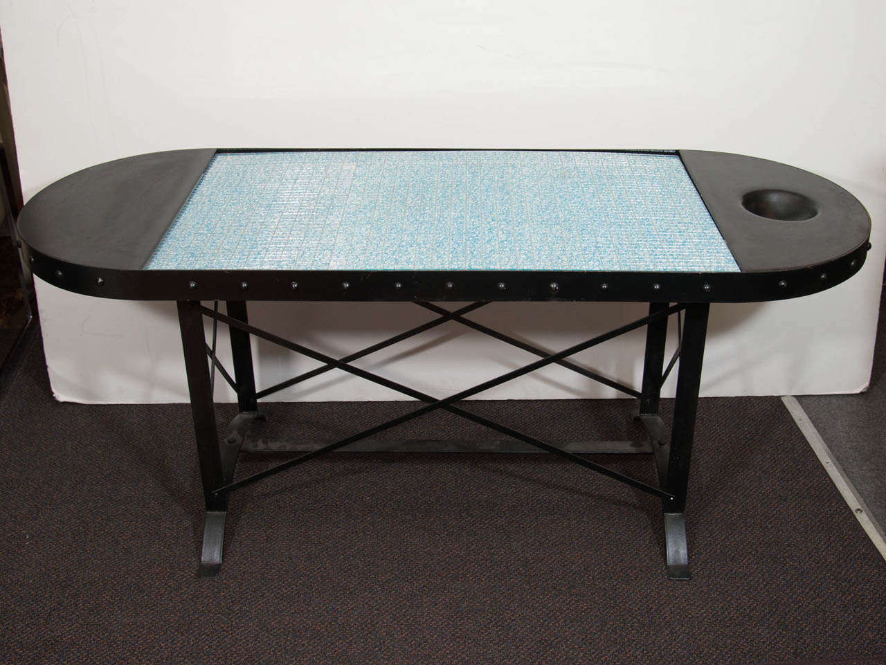 A vintage oblong shaped iron cocktail table with nail head detail.  The top is decorated with a rectangular glass section.The glass consists of smaller rectangular pieces of mirrored glass that are embellished with an applied bright blue swirl