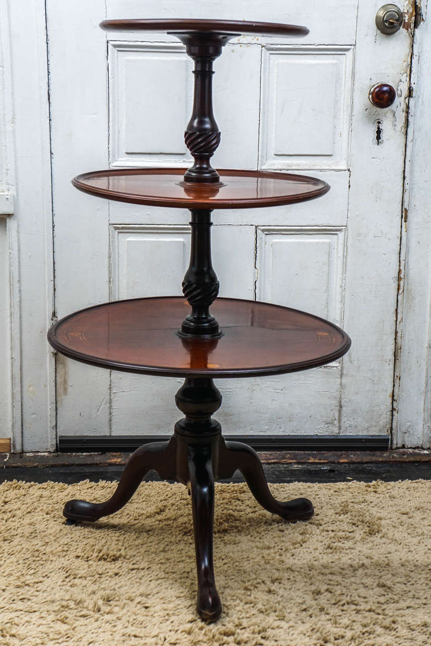 This piece made in an 18th century Georgian  style was crafted in the late 19th century. Made from mahogany then inlayed on each level with colored holly and natural boxwood stringing as well as rosewood banding on the top shelf. The inlays form
