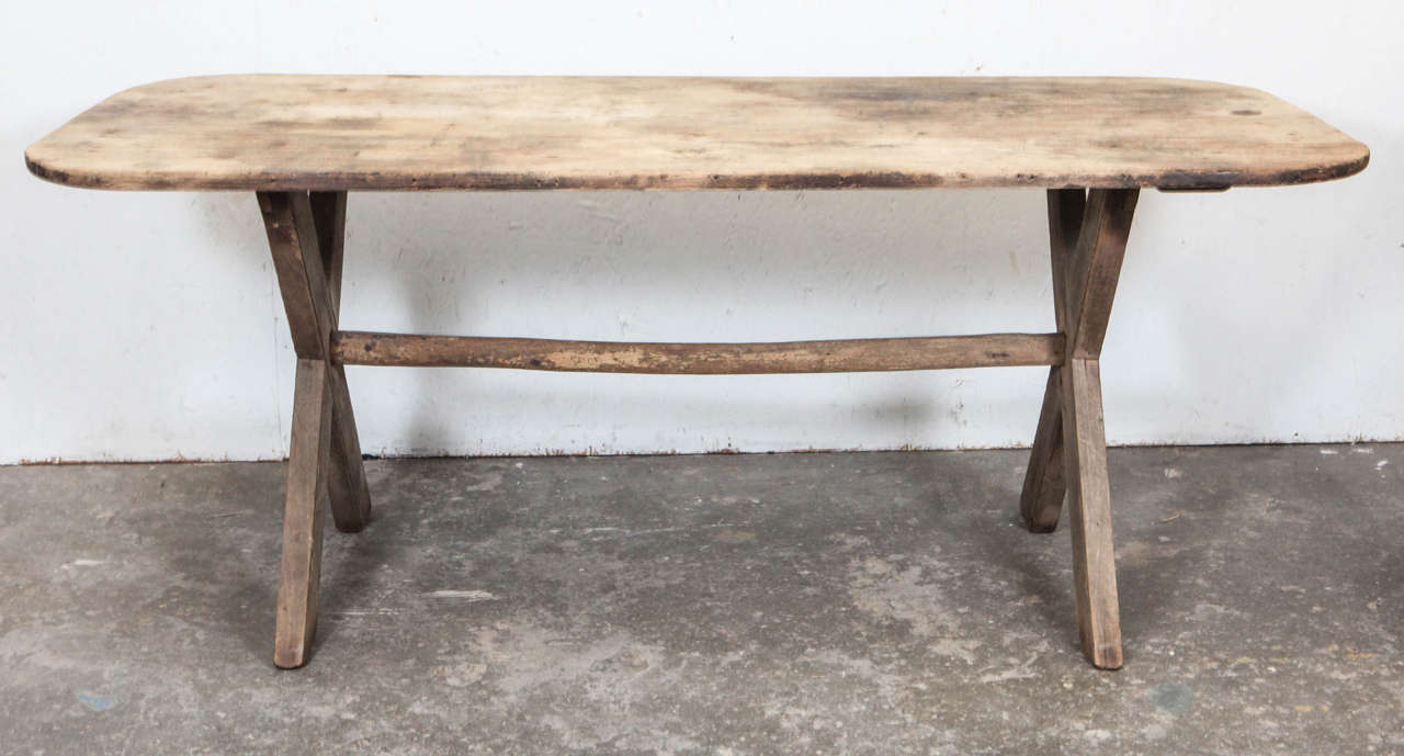 Rustic dining table with X crossed legs and center support. Rounded edges and grey natural fade finish.