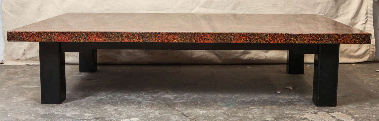 Low coffee table with uniform pattern of red, browns, and greens. Glossy lacquer finish.