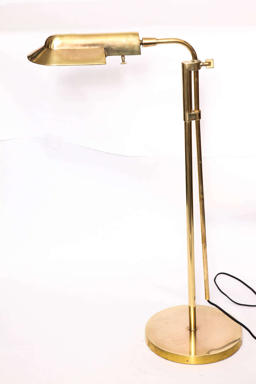 A brass pharmacy floor lamp, produced in the United States, circa 1960s, with rounded shade on curved adjustable stem and circular base. Height may be adjusted, between 32