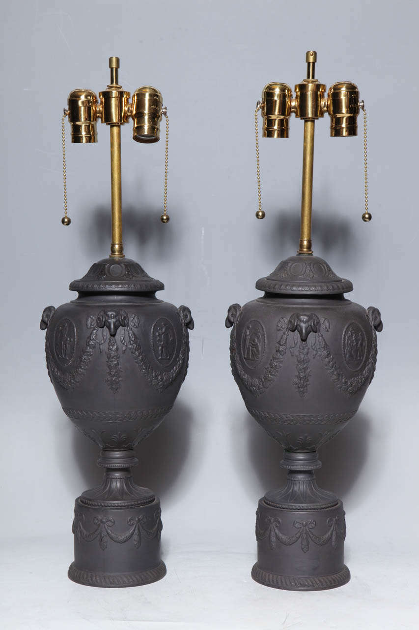 A fine pair of antique English black basalt neoclassical covered urns as lamps. This neo-classic style pair of black basalt ram's head decorated vases on plinths, was inspired by the empire period, which in turn was inspired by the excavations in