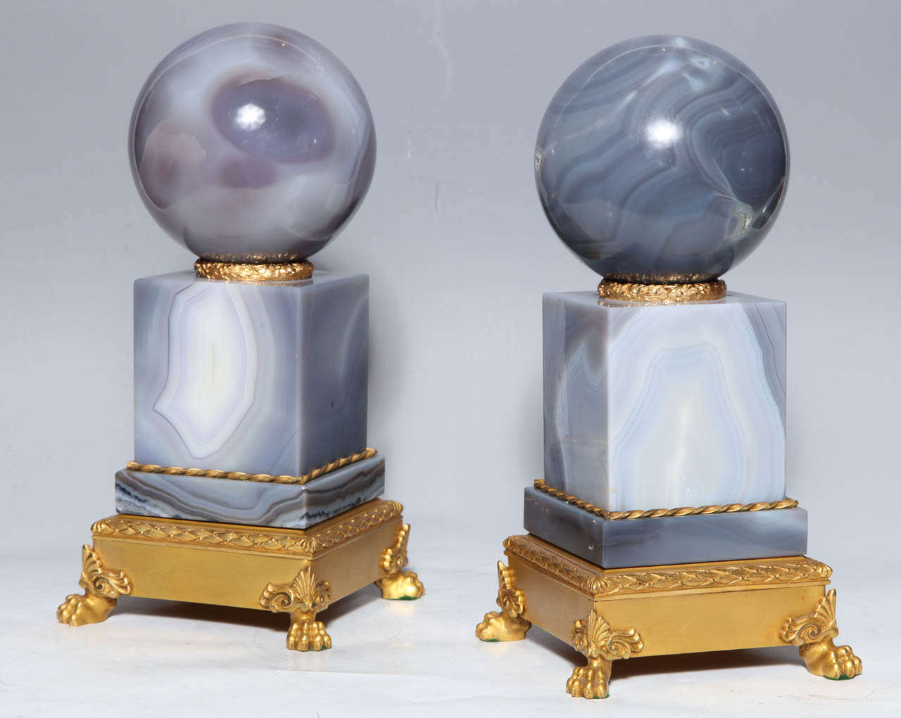 This pair of second empire style agate orbs on plinths have lions claw feet of gilt bronze with mounts of typical neoclassic derivation while the natural markings of polished grey agate give a sense of movement and elegance to these decorative