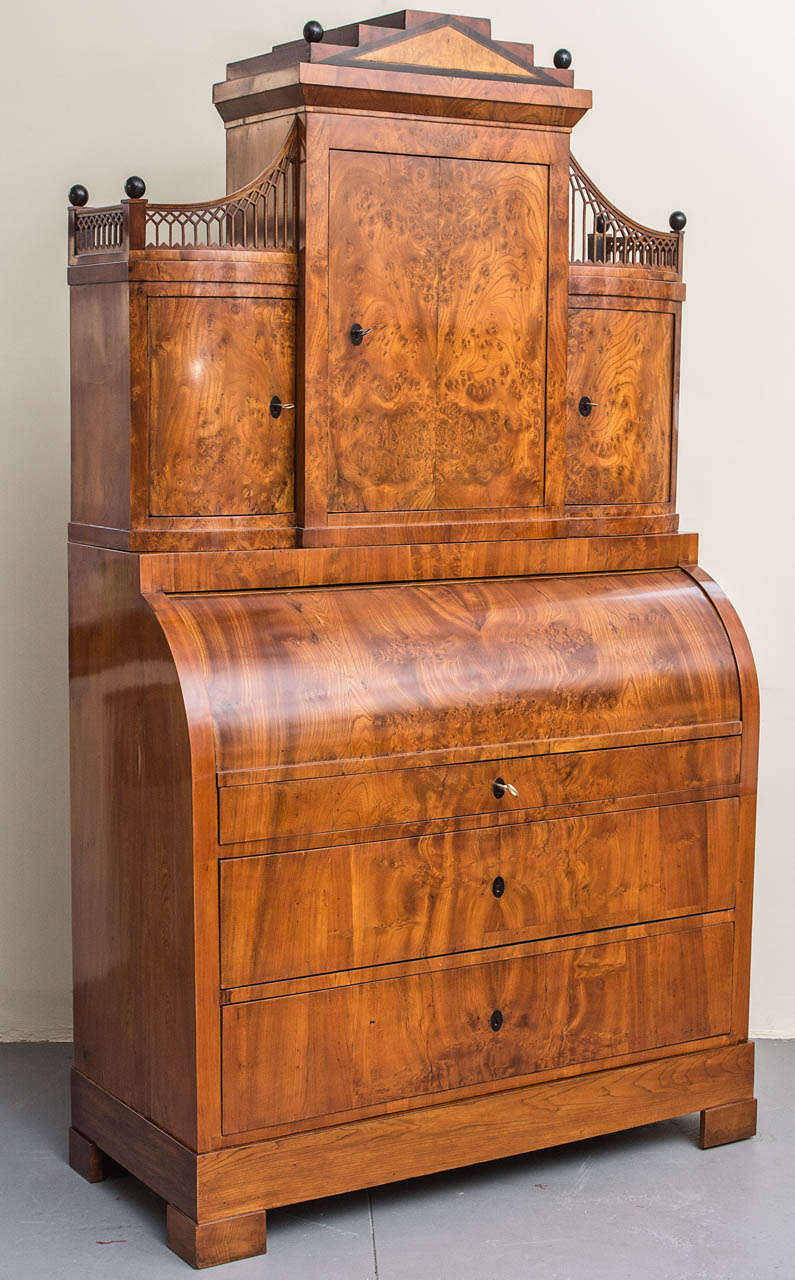 A Fine Danish Empire Cylinder Secretaire, Early 19th Century, elmwood, elm root, birch, fruitwood and ebonized; the top part with a central door flanked by curved doors and surmounted by a pieces gallery, ball finials and a stepped top section. The