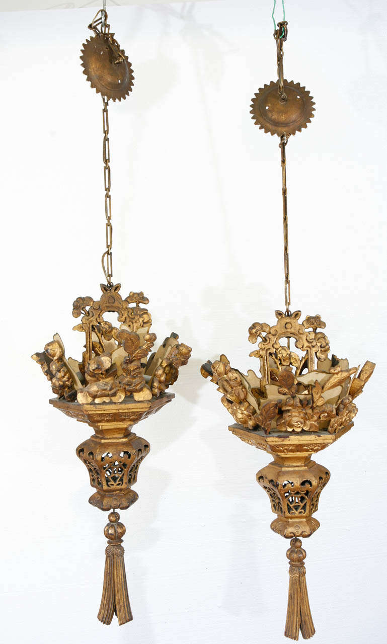 Hand carved, gilt Chinese chandeliers with hand applied gilt finish.  Ornate carvings include floral motif, lace cages and large tassels at the bottom. Original chain and canopy for both. 
Pieces differ slightly in carved designs. Chandelier is 30