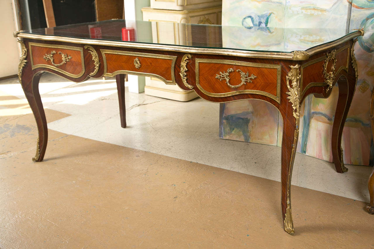 A large and Impressive Bureau-plat in the Louis XV taste. The overall piece having finely cast bronze mounts on a curved front and curved leg structure. The tooled leather top under a half inch piece of glass. The front with three drawers all bronze