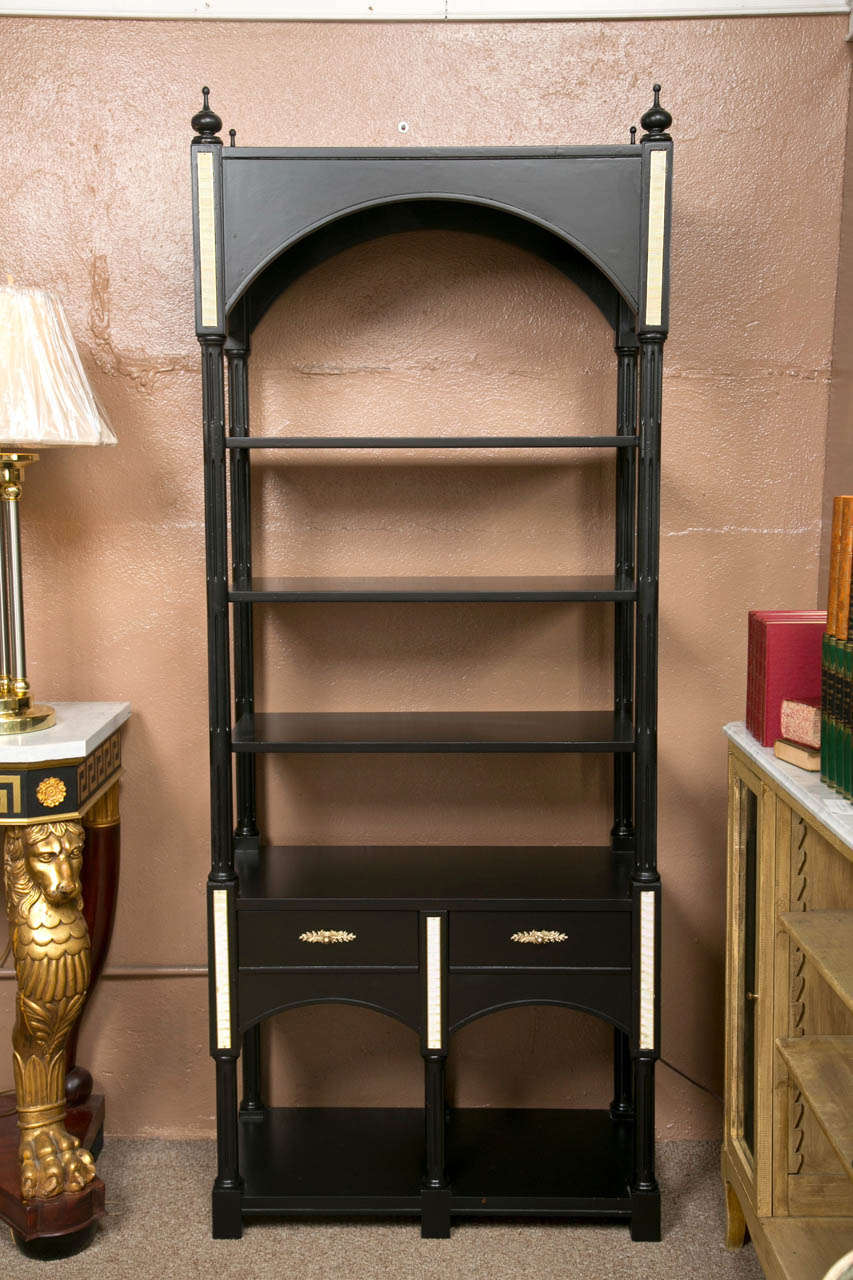 Pair of Hollywood Regency style etagere bookcases, circa 1960s, overall ebonized, each having the top decorated with bulbous finials, the domed top atop three shelves, all over a two drawer compartment, supported on a plinth. The whole with fine