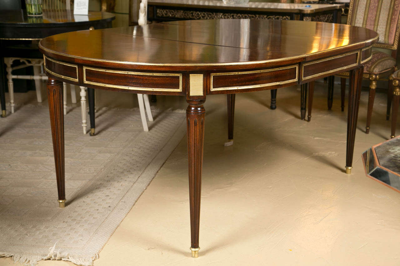 French Louis XVI style mahogany circular dining table, circa 1940s, the parcel-gilt banded top over a narrow and bronze mounted frieze, raised on circular tapering legs ending in capped feet. The apron with cookie corner bronze mounts. Recently
