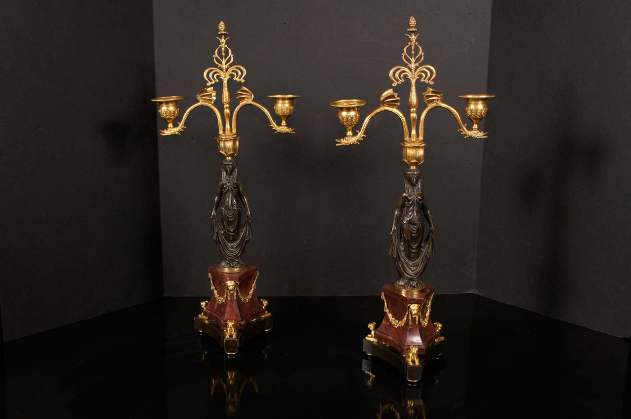 This lovely pair of candelabra, crafted in both gilded and patinated bronze, are 19th century French. Cast as female figures in Egyptian headdress and classical robes standing upon Rouge Royal marble plinths decorated with regal lion heads and