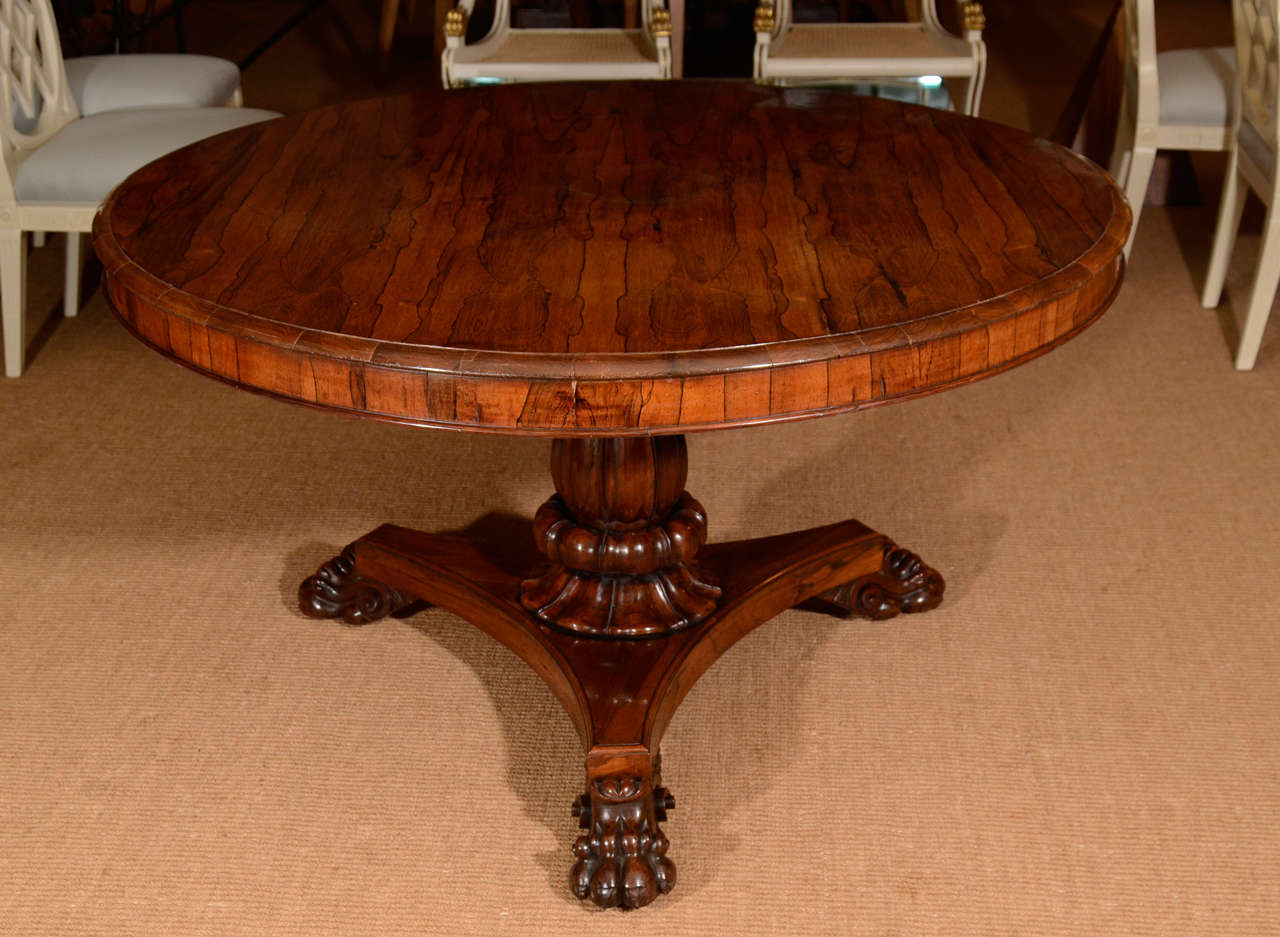 The circular rosewood top with cross-banded edge over a molded frieze. The table top on a leaf-carved center pedestal ending on a concave sided tripartite base, supported by scroll and leaf-carved paw feet.