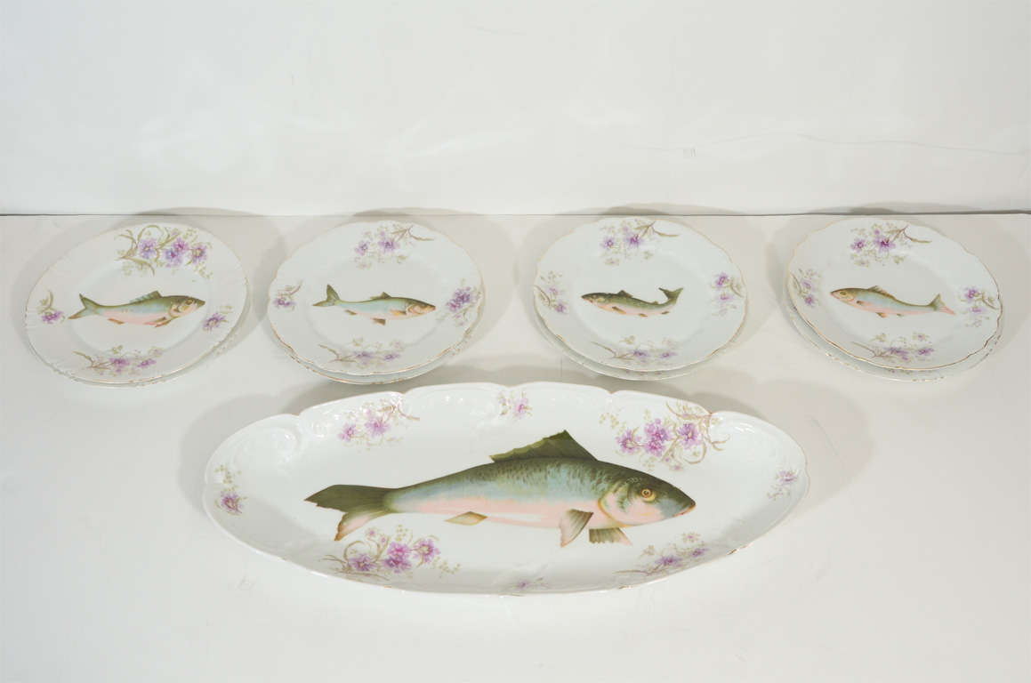 This handsome porcelain dining set features a large rectangular platter with 8 smaller round dessert/serving plates. Each piece features a European chub fish in the center of dish replete with shades of moss, rose and sky blue. There is a floral