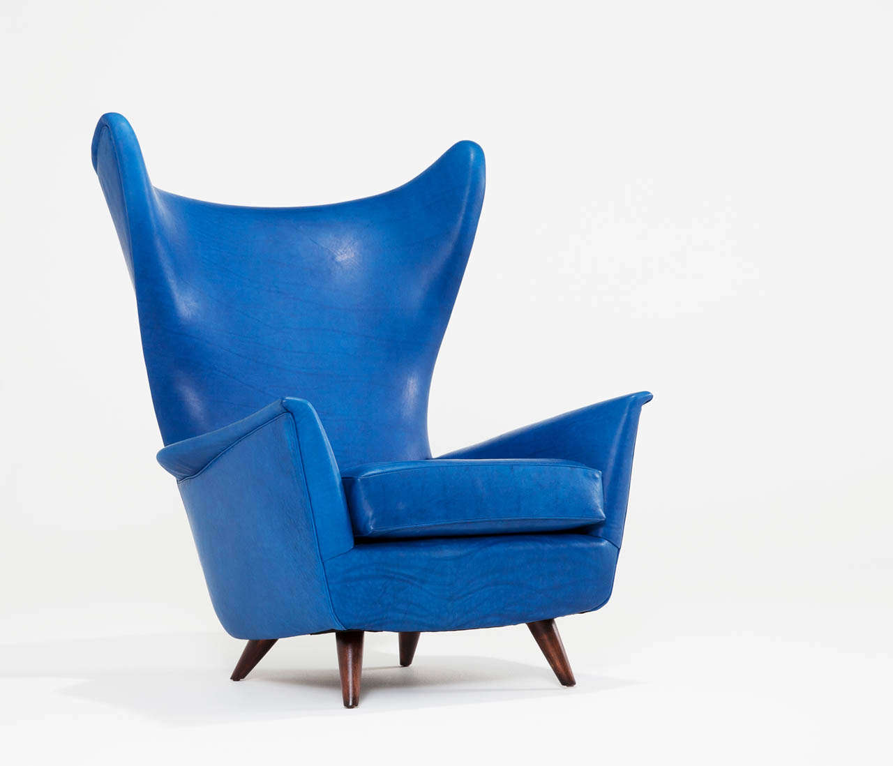 Interesting shaped Italian midcentury wingback chair completely reupholstered in high quality Sapphire blue leather, or can be reupholstered to any fabric of your choice. 

Very elegant shapes which are emphasized by the slim design and the unique