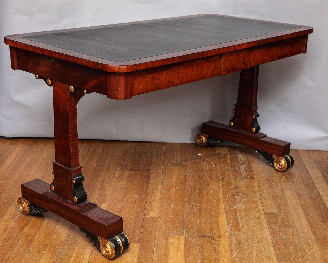 An English late Regency sofa table/desk with vertical supports having ebonized and gilt details. The top finished on four sides, and having two drawers in apron on one side and false drawers on the opposite side. The surface with inset leather top