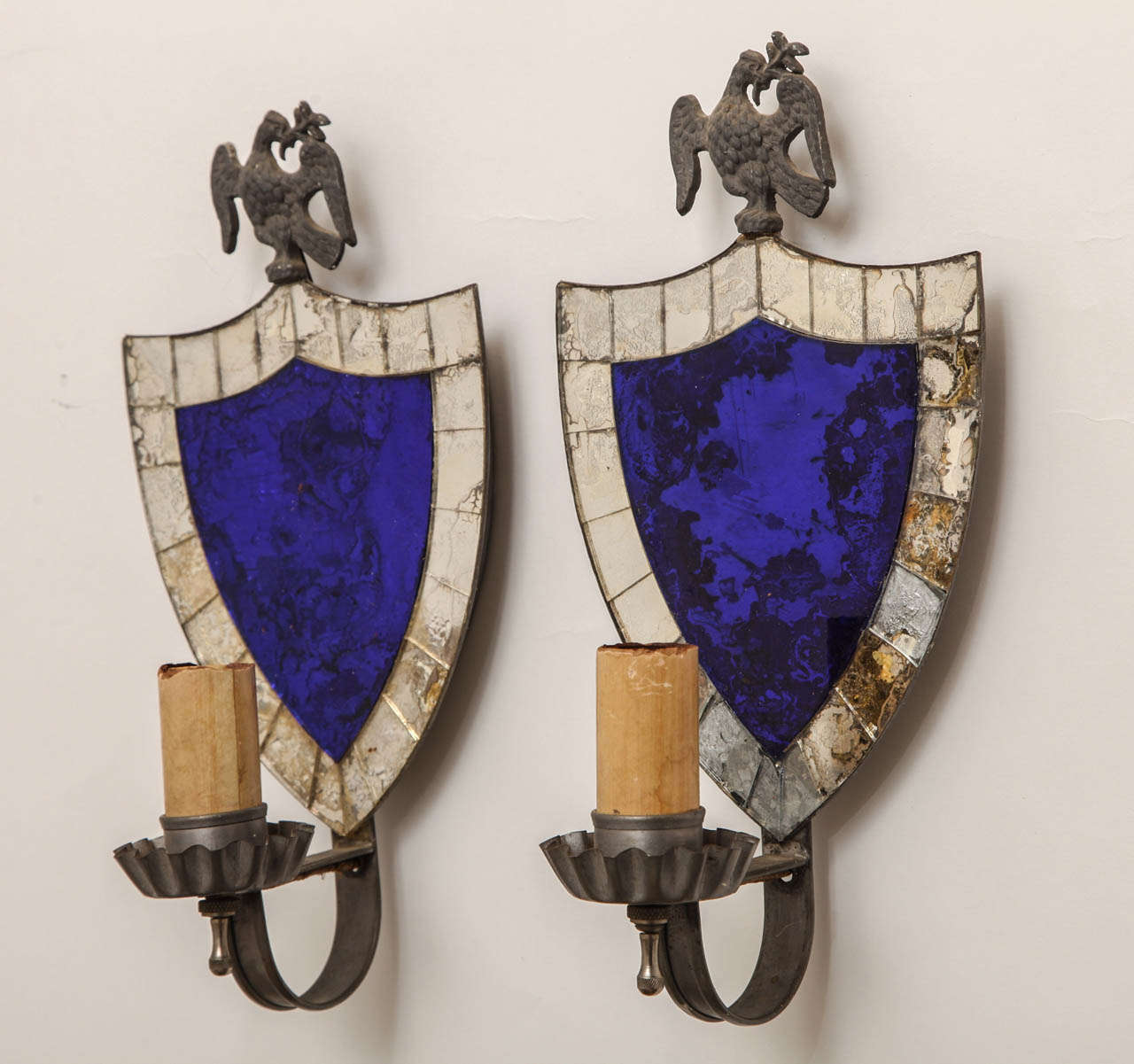 A pair of English shield back sconces. The cobalt center glass surrounded by sections of silvered glass behind single candle arm. The shield surmounted by eagle motif ornament.