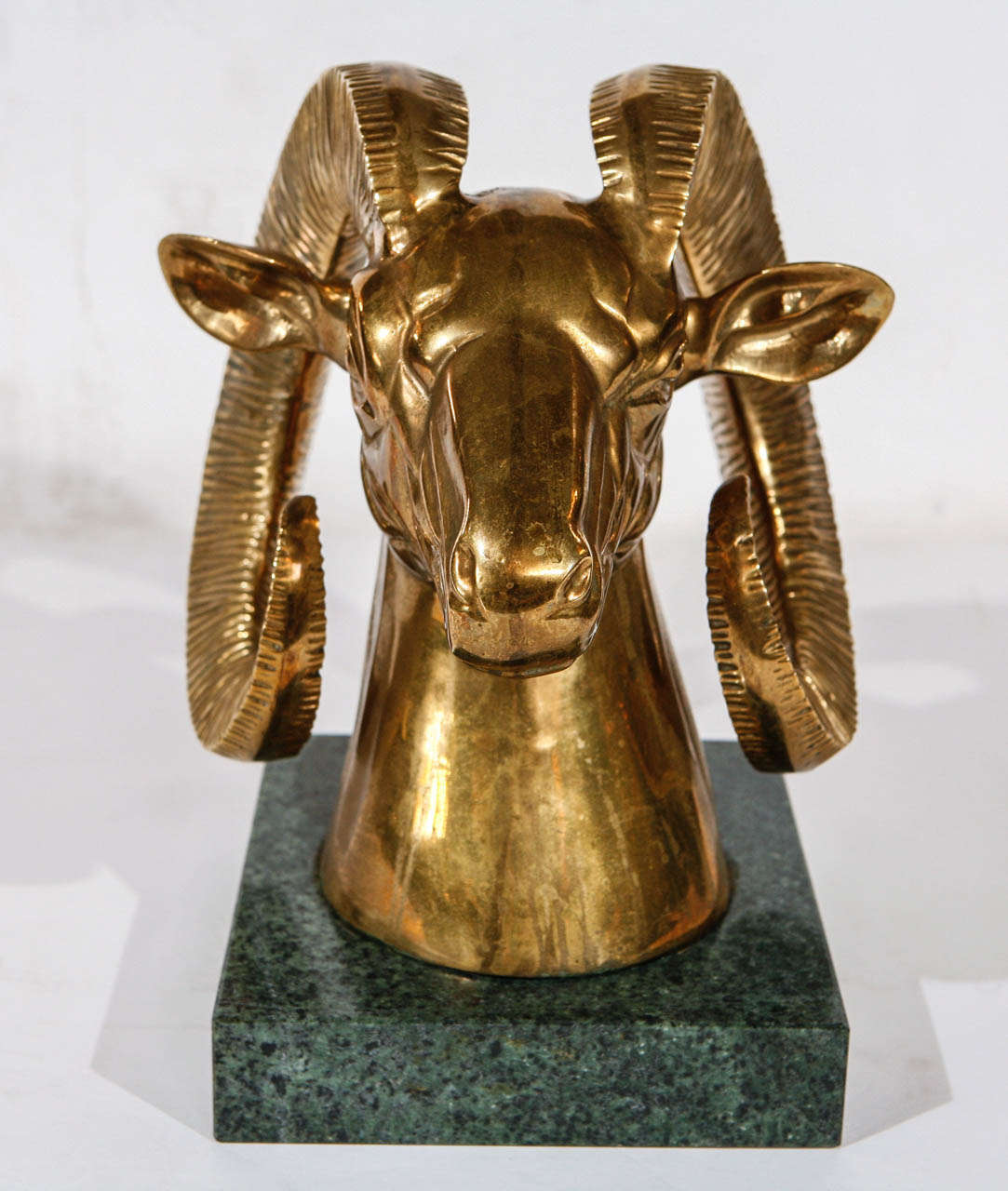 A large size Hollywood Regency brass ram's head mounted on a green marble base.